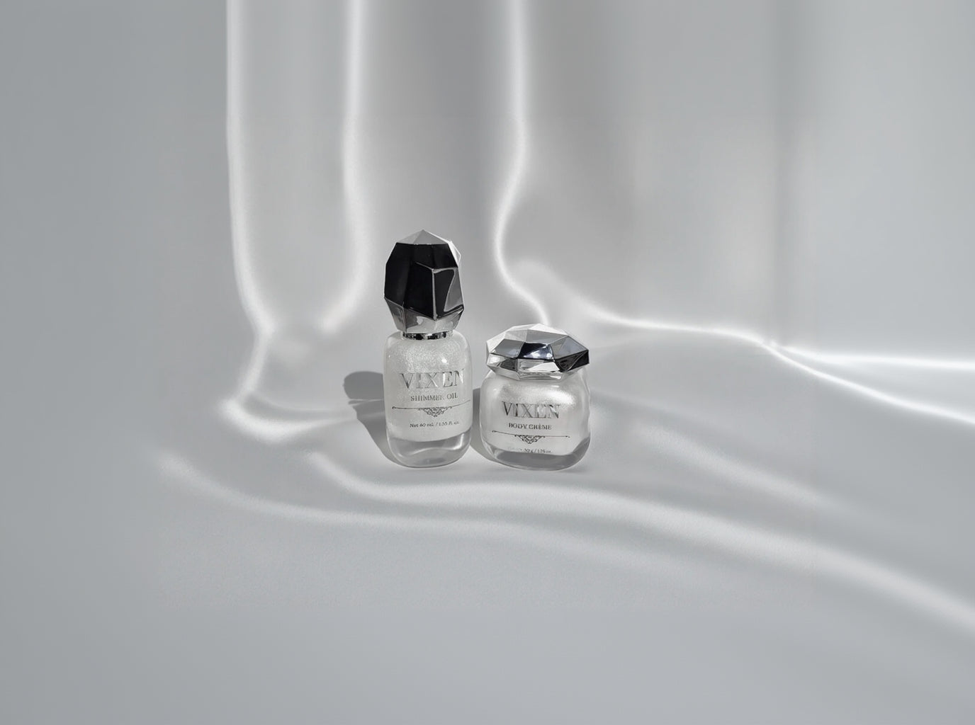 Two skincare products with metallic caps on a satin surface