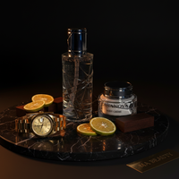 Bottle of Casanova Body Oil, jar of Casanova body crème, watch, and sliced oranges on a dark marble tray.