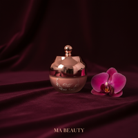Rose gold beauty product with a pink orchid on a dark red fabric background, featuring 'MA BEAUTY' branding.