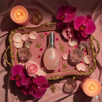 Perfume bottle on a decorative tray with flowers and candles on a pink fabric background